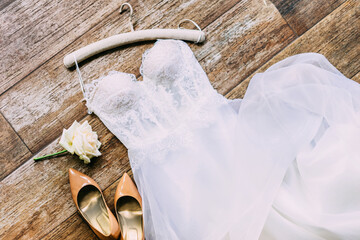 Lay flat of wedding dress, rose and beige shoes on the wooden background