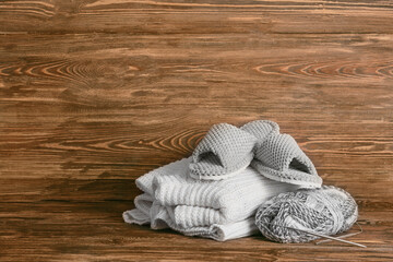 Pair of soft slippers, clothes and knitting threads on wooden background