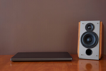 Work place - laptop and music speaker. Wooden table. Background brown wall with copy space.