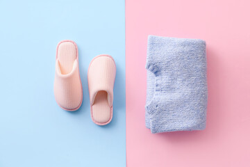 Pair of soft slippers and clothes on color background