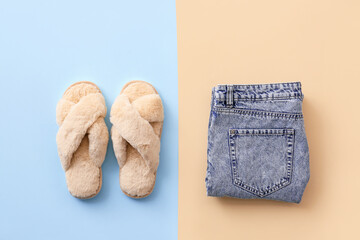 Pair of soft slippers and clothes on color background
