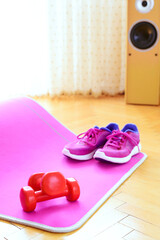 Low angle view of pink mat for workout, two red dumbbells and workout shoes - on wooden floor. Home training.