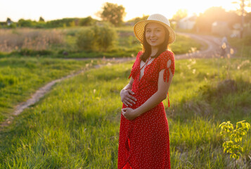 A young pregnant brunette woman walks outdoor on a sunny summer evening.