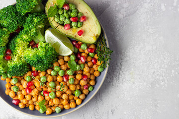 Healthy vegetable lunch of broccoli, roasted chickpeas, avocado, green peas, pomegranate seeds, lime and mint on a ceramic plate. Vegan food, clean eating or dieting concept. Top view.