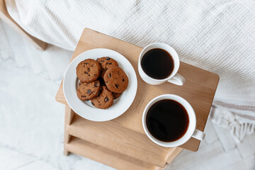 Breakfast in bed. Hot coffee with oatmeal cookies with chocolate on a wooden tray.
