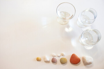 Three glasses of water, a heart shape and colorful stones on a white table. The heart shape created by light, shadow and glass of water.