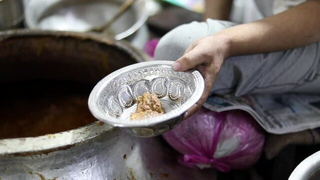 Putting famous nihari into a silver traditional bowl from a huge copper pot at an Indian street food restaurant.