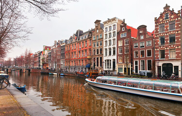 Naklejka premium Netherlands. Amsterdam. Tourists ride a pleasure boat along the Heerengracht canal and admire typical Dutch buildings with traditional pediments on spring day. Beautiful Holland cityscape