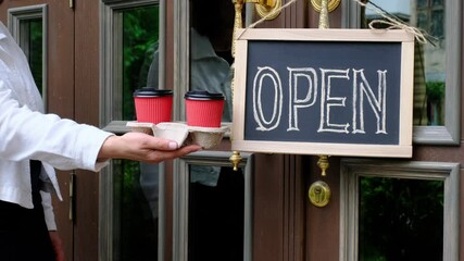 Woman's hands holds two cups of coffee near dashboard with text open. Worker shows advertising opening of the cafe or restaurant.