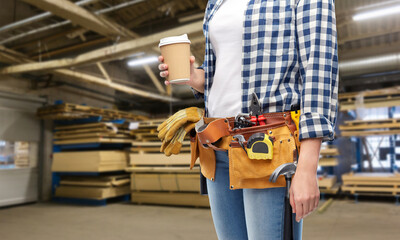 industry, production and job concept - female worker or builder with takeaway coffee cup and working tools on belt over workshop background