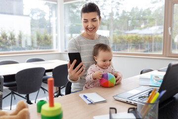 remote job, multi-tasking and family concept - happy smiling mother with baby, smartphone and...