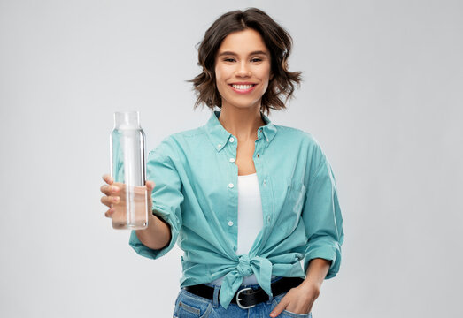 People Concept - Portrait Of Happy Smiling Young Woman In Turquoise Shirt Holding Water In Reusable Glass Bottle Grey Background