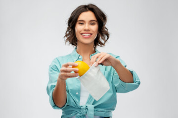 sustainability, eco living and people concept - portrait of happy smiling young woman in turquoise shirt putting orange into reusable bag over grey background