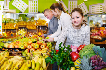 Obraz premium Preteen girl choosing ripe fruits and vegetables in greengrocery