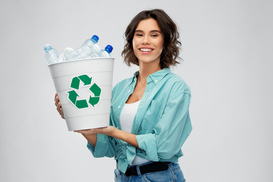 recycling, waste sorting and sustainability concept - smiling young woman in striped t-shirt holding rubbish bin with plastic bottles over grey background