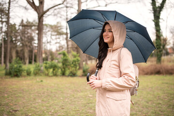 Life style, travel concept.Model under rain. summer woman in the park during a rainy and gloomy day walks in the park and carries an umbrella