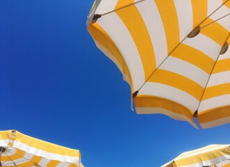 Low angle bottom view and detail of yellow and white beach or poolside umbrellas with a blue sky in...