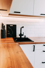 Black faucet and sink. Bright kitchen interior. White modern dining room. Wooden complete kitchen with gas oven