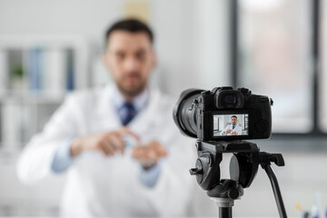 healthcare, medicine and blogging concept - male doctor with camera and hand sanitizer recording video blog at hospital