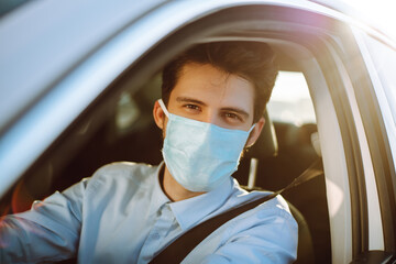 Fototapeta na wymiar Young man in protective sterile medical mask sits in the car during an epidemic in quarantine city. Health protection, safety and pandemic concept. Covid - 19.