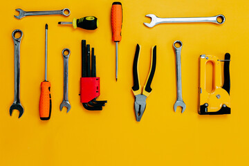 Tools top view on yellow background. Plier, open wrenches, screwdrivers and staple gun flat lay...