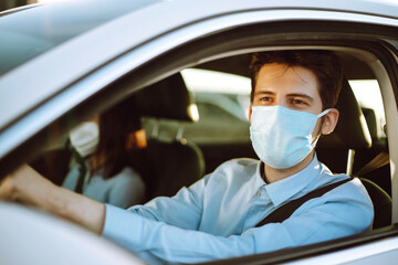 Fototapeta na wymiar Young man in protective sterile medical mask sits in the car during an epidemic in quarantine city. Health protection, safety and pandemic concept. Covid - 19.
