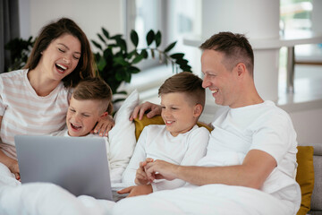 Obraz premium Young family watching movie on lap top. Beautiful parents with kids enjoying at home. 