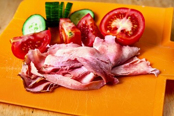 Ham, tomatoes and cucumber on kitchen board.