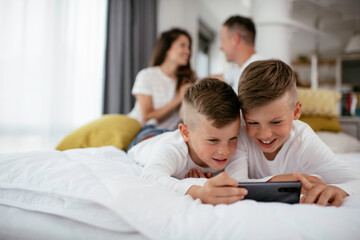 Two little brothers are playing games on the phone. Beautiful boys enjoying at home.