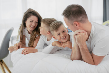 Young family enjoying in bed. Happy parents with sons relaxing in bed.	