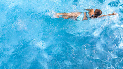 Active young girl in swimming pool aerial top view from above, child relaxes and swims on inflatable ring donut and has fun in water on family vacation, tropical holiday resort
