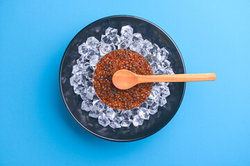 Bowl of red caviar on vintage black metal tray with ice over bright blue background. Top view, copy space, flat lay.