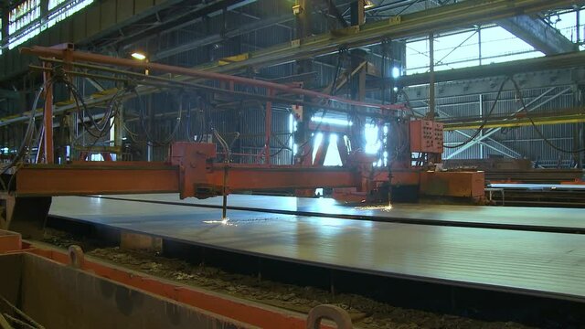 Panning wide shot. Dual oxy gas cutting machine slices steel plates at a steel mill.