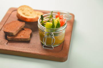 Plate with fresh vegetables and thick sauce in a jar, with different kinds of bread, served on a rustic wooden board.