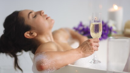 Sexy girl relaxing with wine in bathtub. Woman holding champagne in bath