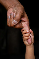 Fototapeta premium A baby's hands holding tightly A senior man's old age finger. Family, Generation, Support and people concept. Dark background.