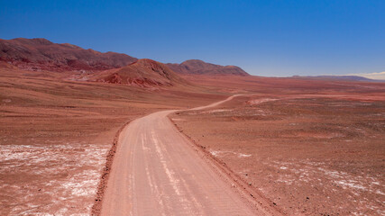 Aerial shot of desert red dirt road winding away into the distance beside some bare rocky hills and mountains