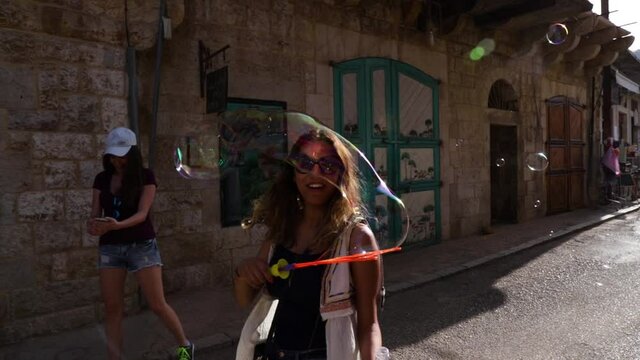 Caucasian Lebanese women friends playing with bubbles on village street, Douma, Lebanon, close up pan