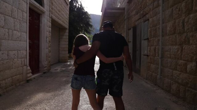 Two Caucasian Lebanese friends walking together crisscrossing their legs in narrow city stone alleyway, Douma, Lebanon, close up circle pan