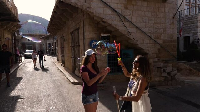 Caucasian Lebanese friends playing outside with bubbles on village street, Douma, Lebanon, close up pan