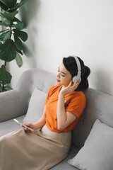 Obraz premium Happy young woman with earphone dancing and listening to music on sofa