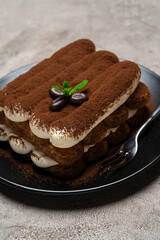 Classic tiramisu dessert on ceramic plate on light grey concrete background