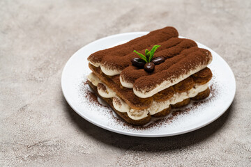 Classic tiramisu dessert on ceramic plate on light grey concrete background