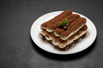 Classic tiramisu dessert on ceramic plate on dark concrete background