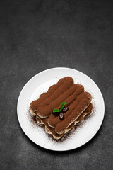 Classic tiramisu dessert on ceramic plate on dark concrete background