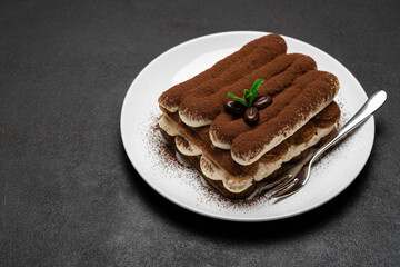 Classic tiramisu dessert on ceramic plate on dark concrete background