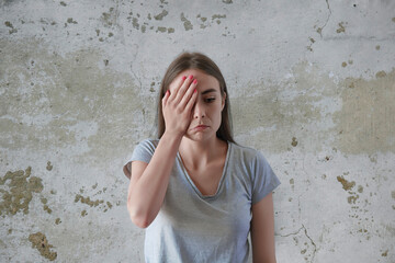 Sad woman near wall background holding her head with her hand