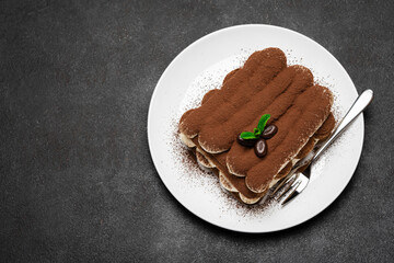 Classic tiramisu dessert on ceramic plate on dark concrete background