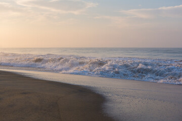 Beautiful seascape shot of the Indian ocean at sunrise with orange sand, a low tide with big white foamy waves and a blue orange sky on the horizon. Pitiwella beach, Sri Lanka