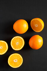 Halved and whole oranges on a black background, top view. Overhead, from above, flat lay. Copy space.